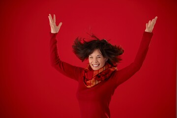 Happy young woman in red autumn clothing posing in front of red background, looking at camera, smiling, hair blown up.