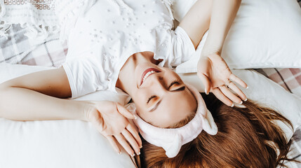Obraz na płótnie Canvas A sleepy brunette girl lies in bed with a blindfold waking up in the morning. Cozy home morning in cute pajamas. Have a good time, relax and dream. Healthy sleep.