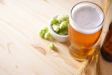 Hops and light beer on wooden background, place for text.