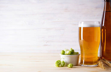 Hops and light beer on wooden background, place for text.
