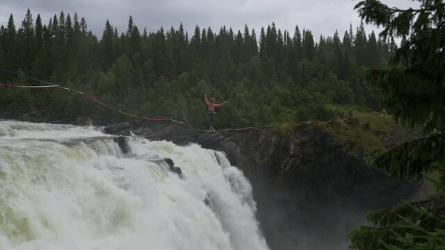 Tannforsen waterfall, Sweden - 08/29/2020: Man walking a tightrope across Tannforsen waterfall in Sweden