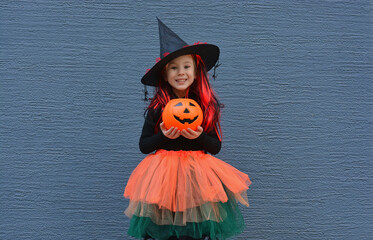 Halloween trick or treat. Portrait smiling girl in witch hat against a blue wall . Copy space for...