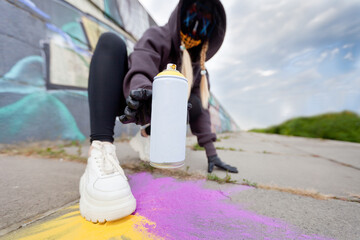 Girl writer, street graffiti in a mask tries to take a spray of paint. Day. Cloudy. Natural light....