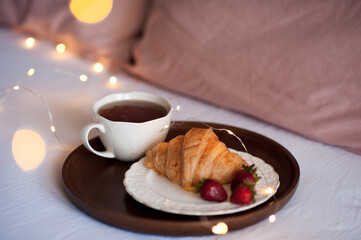 Cup of fresh black tea staying on open paper book over Christmas glowing lights close up. Good morning. Breakfast. Winter holiday season.