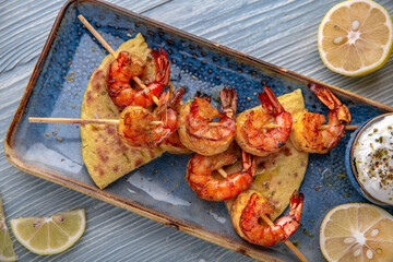 Souvlaki grilled shrimp on skewers. Natural delicious food. Greek cuisine menu. Still life in a marine style on a blue background.