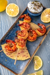 Souvlaki grilled shrimp on skewers. Natural delicious food. Greek cuisine menu. Still life in a marine style on a blue background.