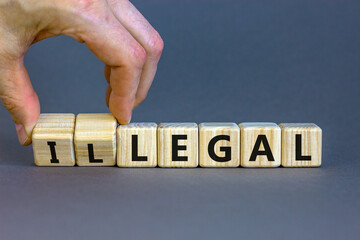Male hand flips wooden cubes and changes the word 'illegal' to 'legal'. Beautiful grey background, copy space. Business concept.