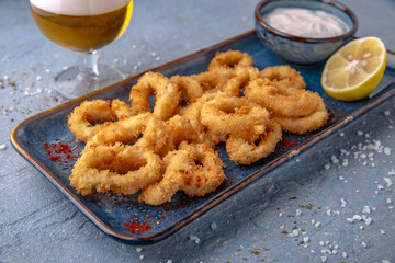 Deep-fried squid or onion rings in batter. Natural delicious food. Greek cuisine menu. Still life in a marine style on a blue background.