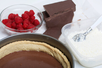 Sponge cake with chocolate ganache. Nearby are raspberries and pieces of chocolate. Levington cake, stages of preparation.