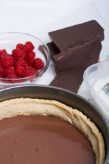 Sponge cake with chocolate ganache. Nearby are raspberries and pieces of chocolate. Levington cake, stages of preparation.