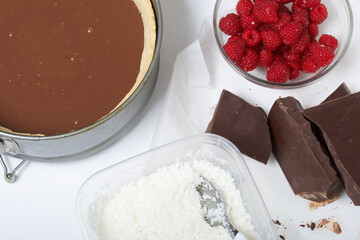 Sponge cake with chocolate ganache. Nearby are raspberries and pieces of chocolate. Levington cake, stages of preparation.