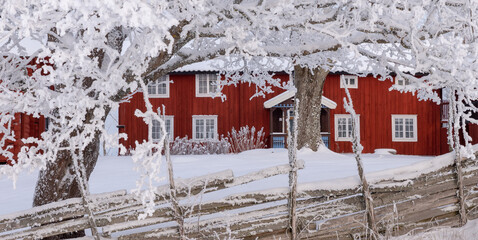 Winter scenery with red cottage surrounded by trees covered with snow and frost.