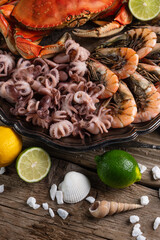 Close-up view of large dish with coked crab, baby octopuses and tiger shrimps served with lemon, lime and seashells on rustic wooden background. Sea delicious. Gifts from the sea. Concept natural food