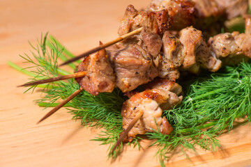 grill meat on a sticks with green on wooden plate