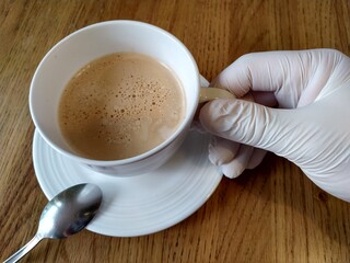 A cup of coffee on a table hold by hand in glove 