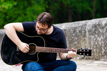 Obraz premium Young man playing guitar sitting on the bridge