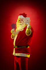 Santa Claus holds playing cards in his hands and poses on a dark red background
