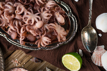 Baby octopuses on a metal dish served with brown napkin, lime, sea salt on rustic wooden background. Sea delicious. Seafood concept. Gifts of the red sea.