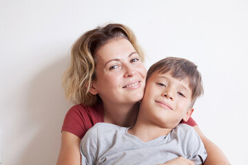 Portrait of happy smiling mom hugging her son sitting on a light background. Happy family concept. 