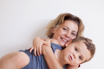 Portrait of happy mother with cute kids boy sitting on a light background. Happy family concept.