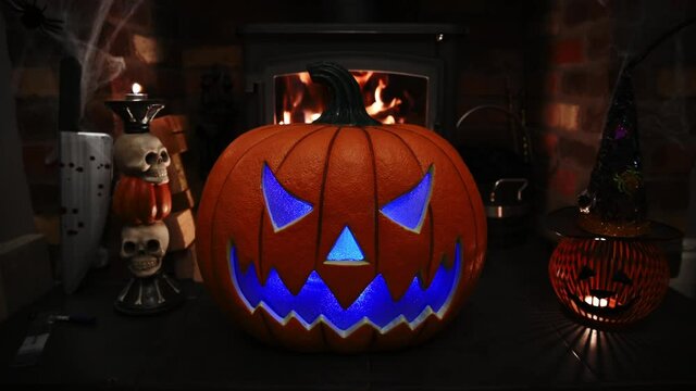4k video of pumpking changing colours on spooky fire place. wram flickering backlight from fire