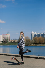 Portrait of a young female in a medical mask with longboard in the city during the quarantine