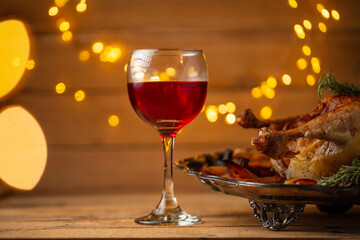 Close-up view of wineglass with red wine on wooden background with yellow lights and dish with baked turkey. Festive dinner. Concept of Thanksgiving day. Food for holiday.