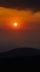 Photo of sunrise over mountains, beautiful orange-red light in the background. Morning fog over the peaks.
