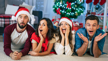 Funny excited beautiful group of friends are lying on the floor and posing on the camera while celebrating christmas holidays at home
