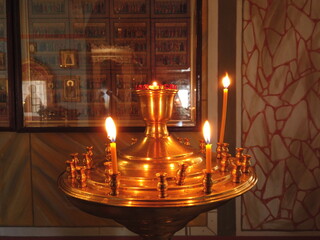 Candles burning on golden stand in front of the saints pictures on the wall