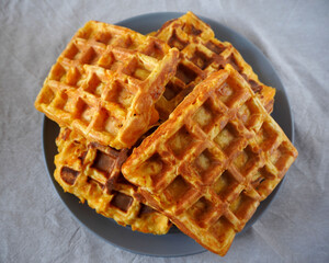 four fresh Belgian waffles made from cornflour, eggs and pumpkin are on the gray round plate on a beige tablecloth a top view. gluten-free homemade food
