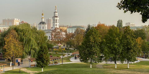 Panorama of the city's children's park with carousels green and yellow trees, in the background an old church and houses, mobile photo