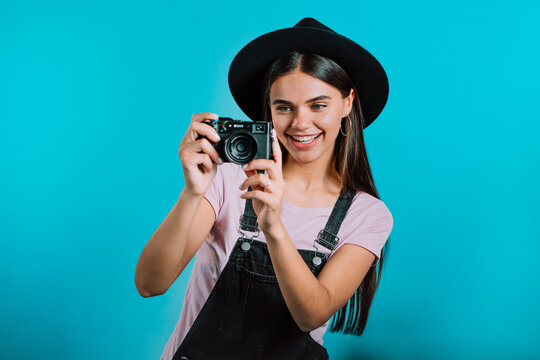 Young pretty woman in overall takes pictures with DSLR camera over blue background in studio. Girl smiling and having fun as photographer.