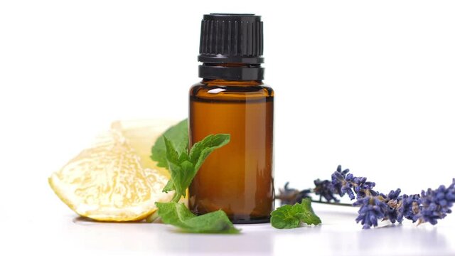 Essential oils in dark glass bottle with aroma herbs. Aromatherapy concept. Fresh leaves of mint, lavender and lemon closeup to jars on white background