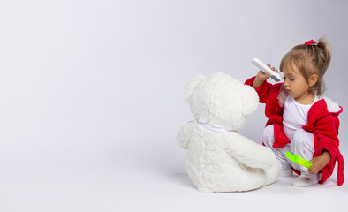 Healthcare concept. Babygirl with bear plush toy. Little girl measures her fever with an infrared...