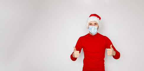 Christmas during pandemic of COVID-19 Coronavirus. Man wearing surgical face mask and Santa hat. Male model wearing red sweater on white isolated background. Place for copy banner text seasonal Sales