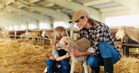 Caucasian cheerful young beautiful mother and small cute pretty girl sitting in stable and caressing lamb. Woman farmer with little girl petting and stroking sheep. Farming. Taking care concept.