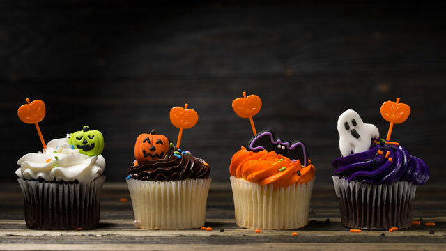 Cupcake dessert on Halloween party. Muffin decorated with colored frosting and Icing shaped pumpkin Jack-o-lantern, ghost and bat. Cupcakes on wooden background.