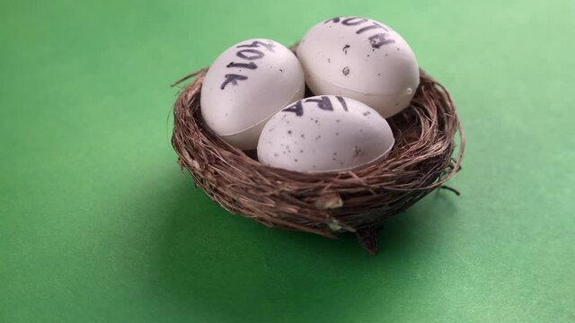 Conceptual composition. Pension savings. Three eggs with the inscriptions IRA, 401k, Roth lie in the nest and rotate against in the green background. Close-up