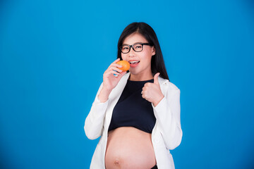 Beautiful pregnant woman in Asia is holding an orange in her hand. On a pink background, expectation of a young mother, pregnancy and childbirth pictures.