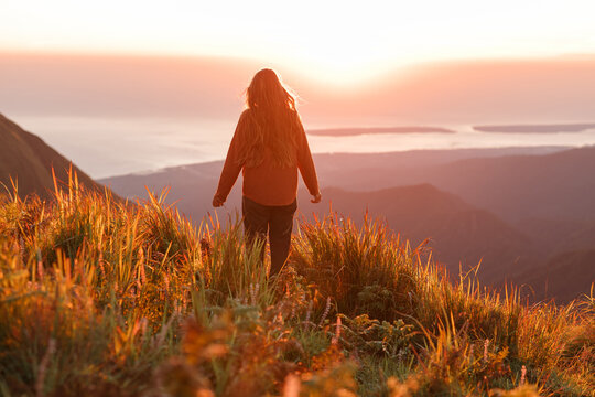 Young carefree woman dressed casual enjoying  desert landscape standing on the mountain top and look sunrise