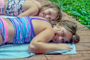Two young sisters tanning on a deck