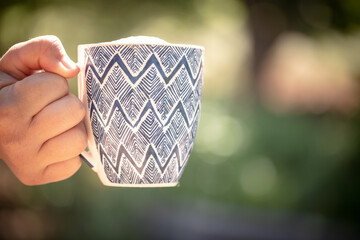 Close up image of woman's hand holding coffee mug with beautiful garden bokeh background