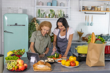 Elderly mother and young daughter getting online cooking class to prepare meal at home. Good family relationship between mom and daughter cooking together