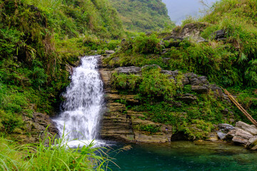 Fototapeta na wymiar The Du Gia waterfall of Ha Giang in northern Vietnam is seen with lush green vegetation at the end of the harvest season in this landscape