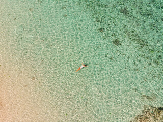 Top aerial view from drone woman in white bikini lying on transparent turquoise water surface on beach. Travel and vacations concept