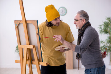 Old man taking lesson from young painter
