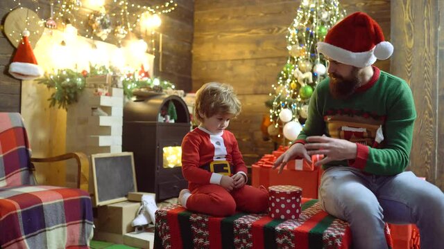 Father and son prepare at Christmas magic. Dad and child open Xmas prasent gifts. Kid with parent in Santa hat enjoy New Year.