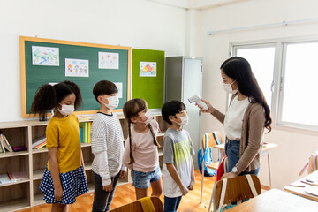 A group of Kids students wearing masks lined up waiting for woman teachers to Check Fever by Digital Thermometer in the classroom for Scan and Protect from Coronavirus Outbreak - Healthcare Concept