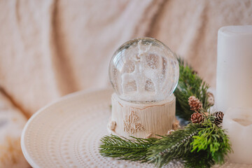 Magic glass snow globe with deer and spruce branches on the bedside table in a light interior.